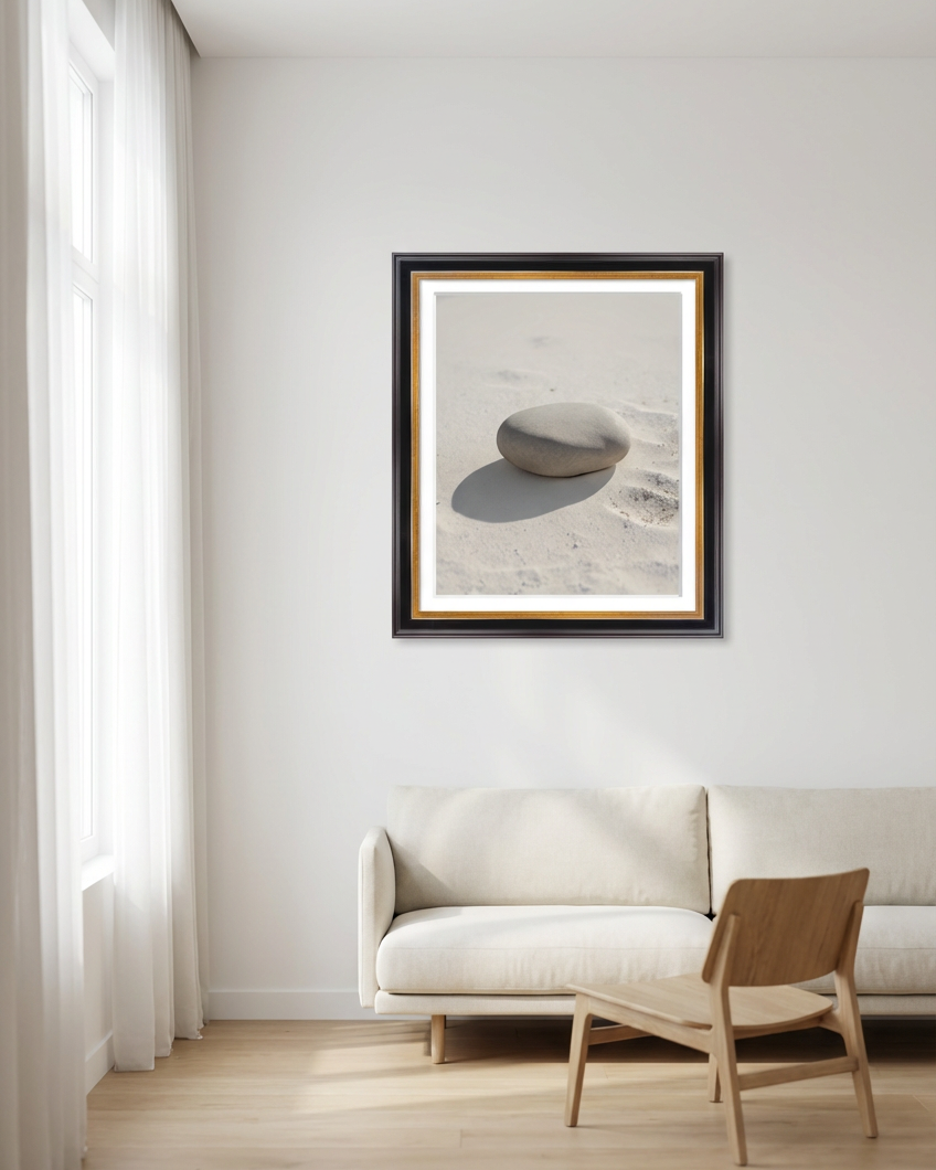 Framed artwork of a stone on a beach wall in a living room with a sofa and chair.